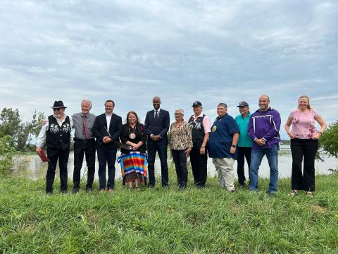 a group of officials stand together in front of a body of water.