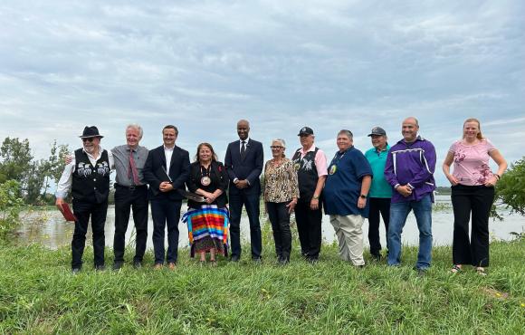 a group of officials stand together in front of a body of water.